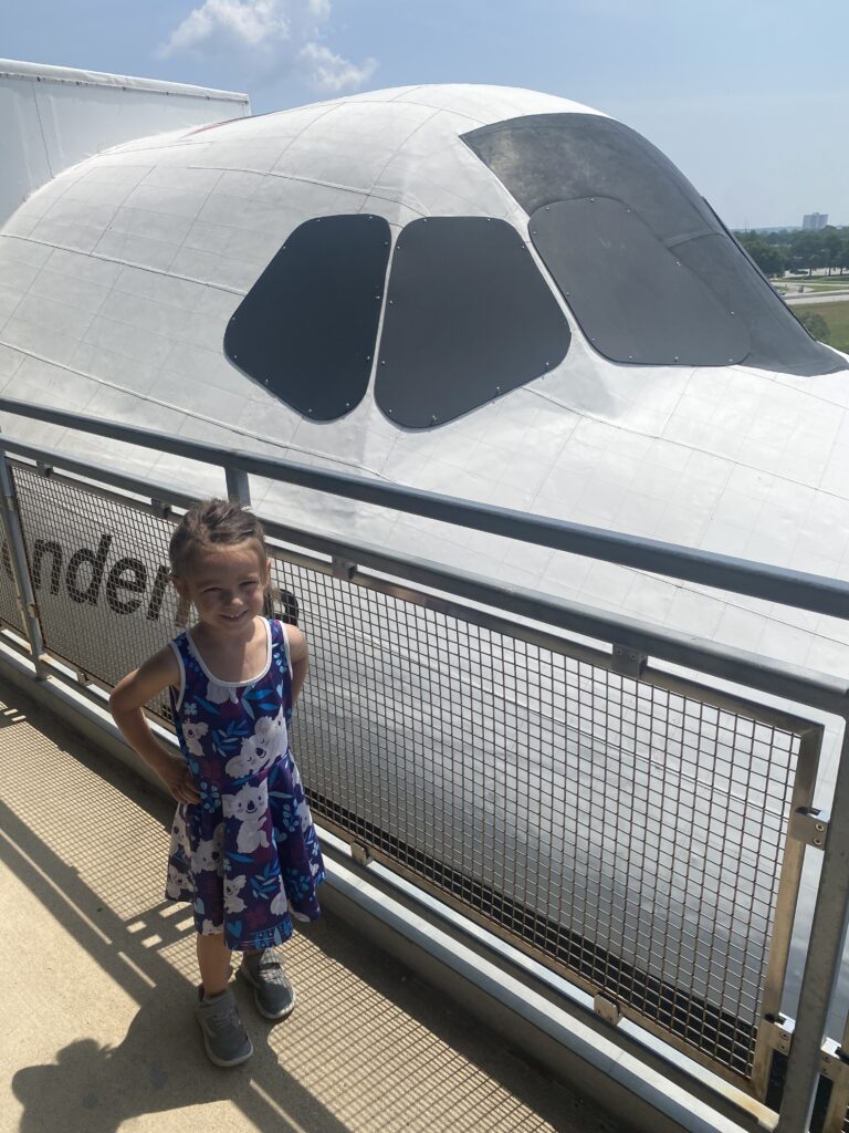 5 year old girl standing next to a space shuttle replica at the Johnson Space Center